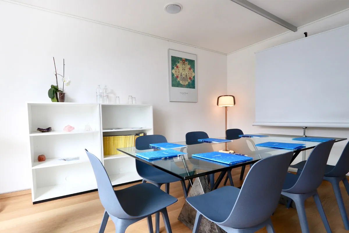 Sala Calicanto: tavolo in vetro con sedie azzurre e schermo